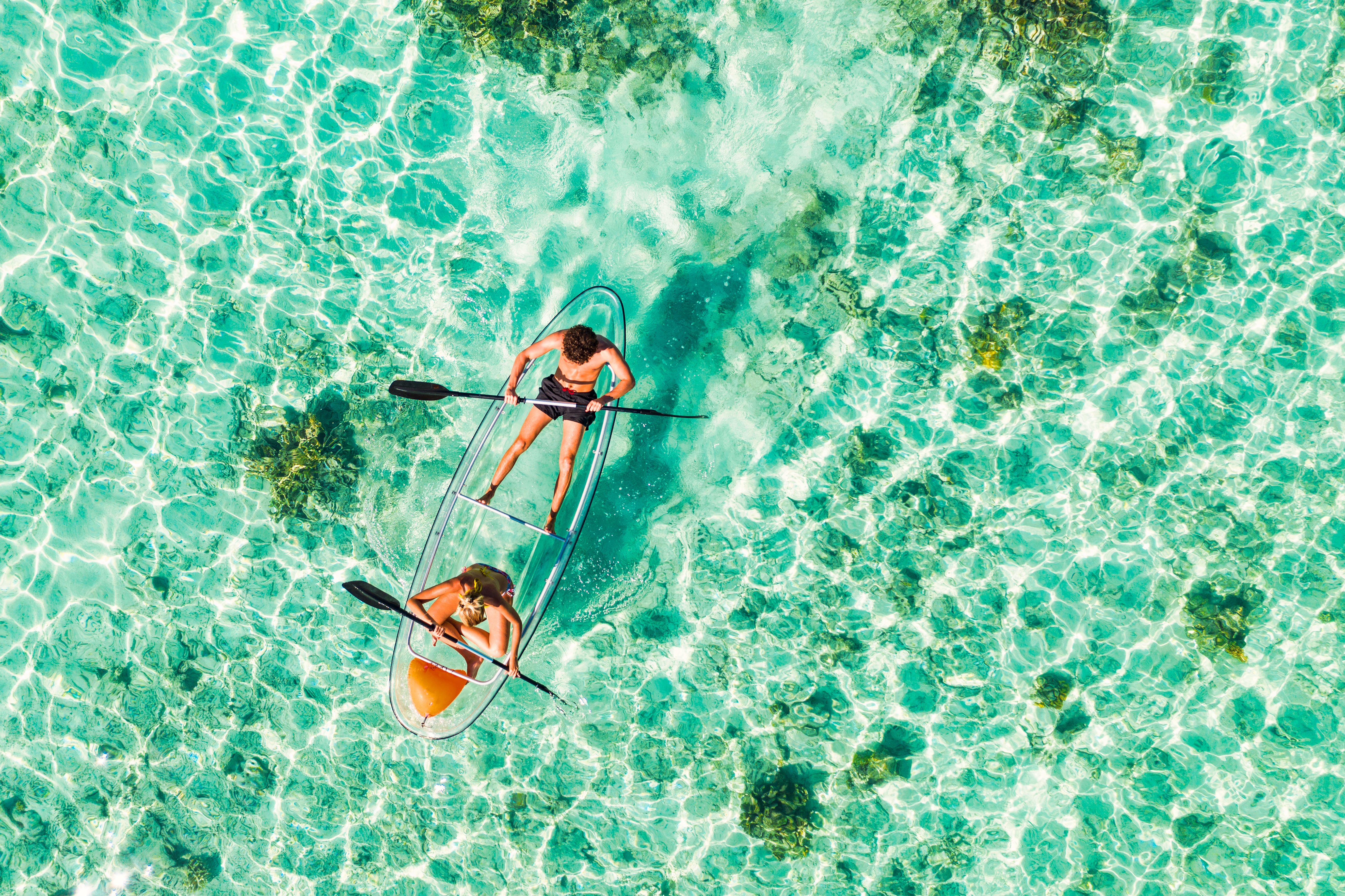 Young couple paddling on glass bottom kayak in tropical ocean